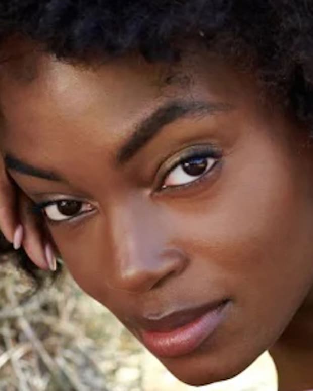 Tanaye White lounges on the ground in a purple bikini and leans her head on her